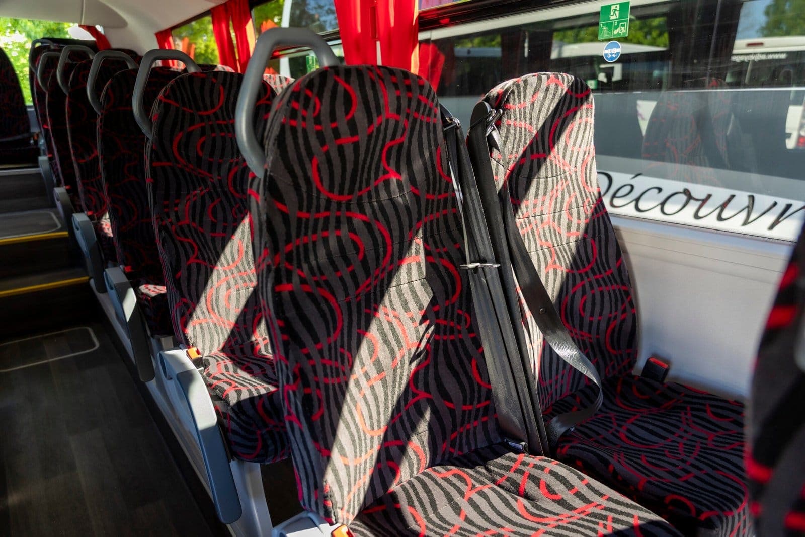 Intérieur d'un autocar scolaire ADJ Voyages avec ses sièges à motifs rouges