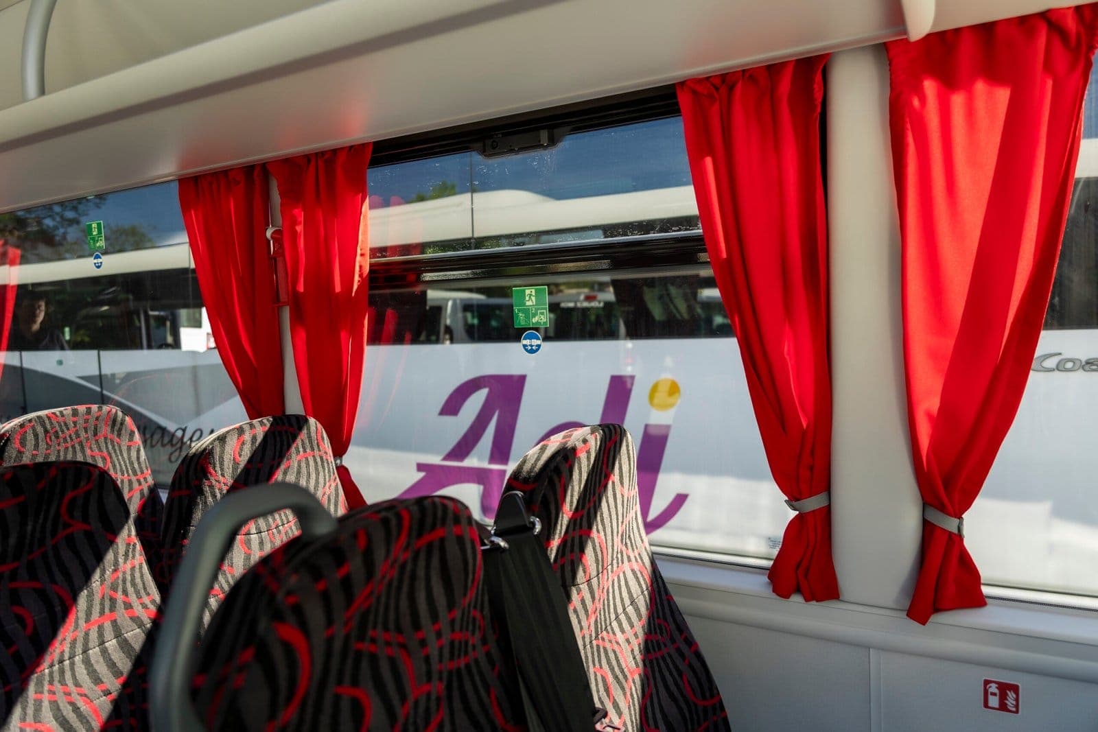 Sièges rouges et rideaux d'un autocar ADJ Voyages